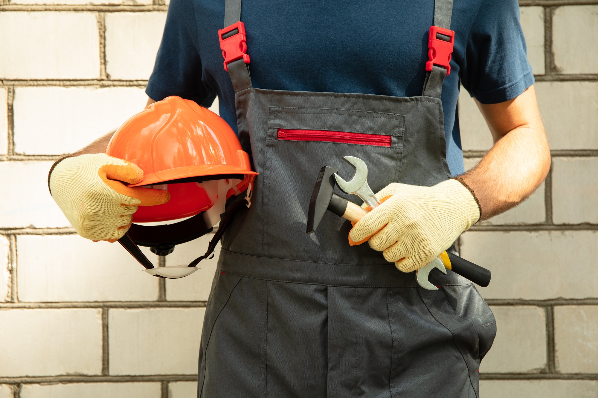 Man in overalls holds safety helmet and construction tools outdoor